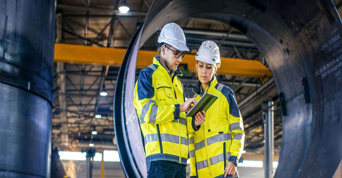 Two engineers reviewing information on a tablet in an industrial facility