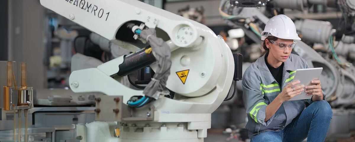 Engineer wearing safety gear, using a tablet near a robot arm