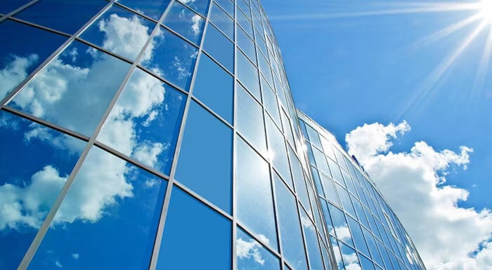 Glass windows of a modern building reflecting clouds and a bright blue sky