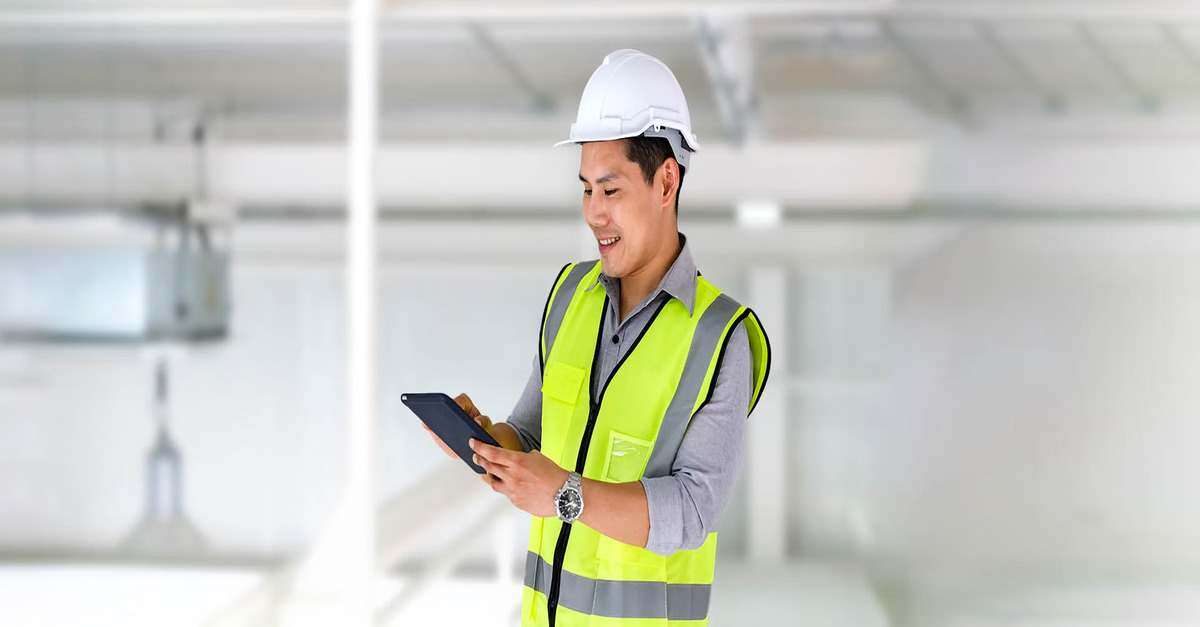 An engineer is holding a tablet, smiling as he works inside an industrial facility