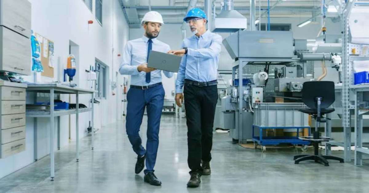 Two engineers in hard hats discussing work while looking at a laptop in an industrial facility
