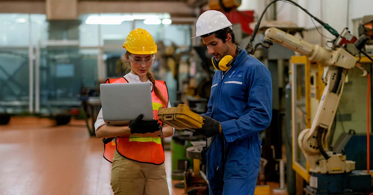 Two workers using manufacturing maintenance software on a laptop