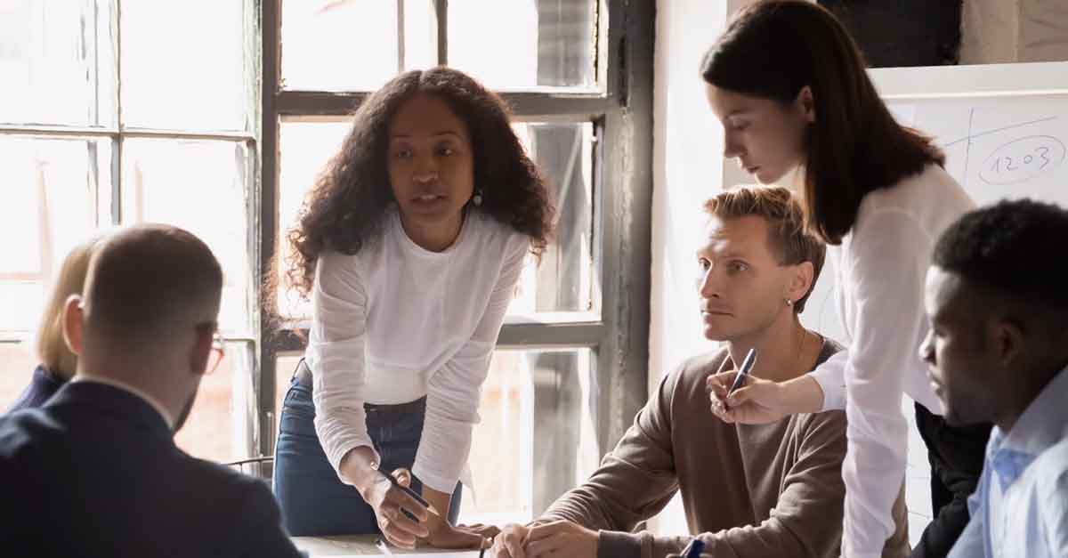 A diverse team engaged in a brainstorming session, with one woman leading the discussion while others actively participate around a table.