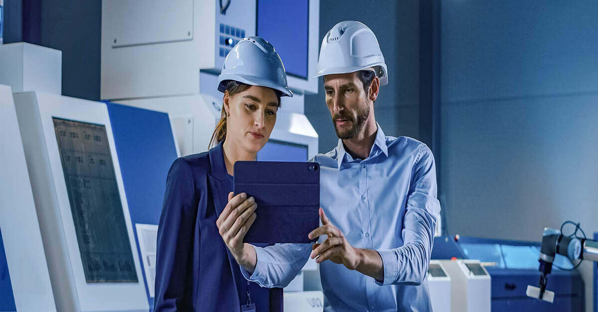 Two engineers wearing helmets, discussing content on a tablet in a high-tech industrial setting