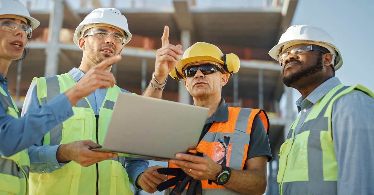 Construction team discussing plans while looking at a laptop on a construction site