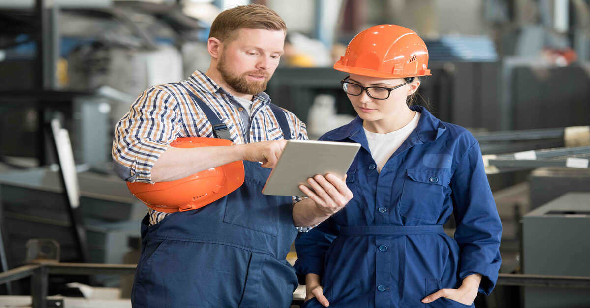 Two workers discussing something on a tablet in an industrial setting